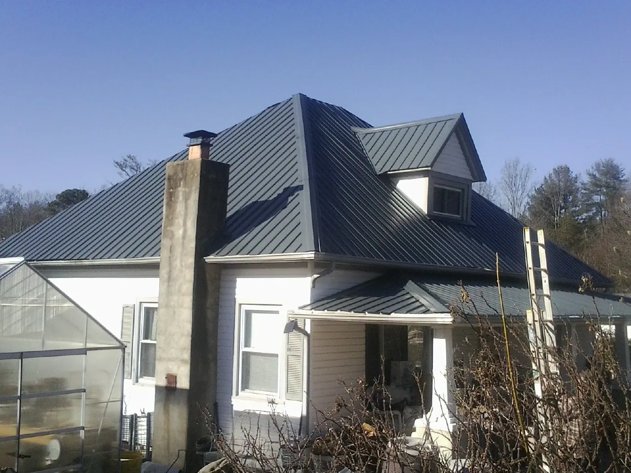 Dark blue standing seam metal roof on a white farmhouse with dormer — Slate & Tile Roof Repair by Roofing Brothers in Battle Creek
