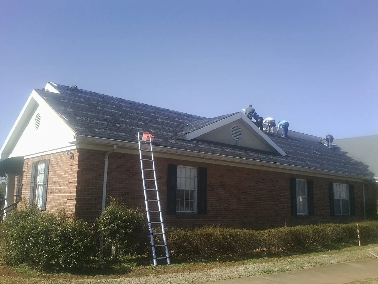 Crew tearing shingles off a brick ranch roof with a ladder set — Metal Roof Repair work by our crew in Battle Creek