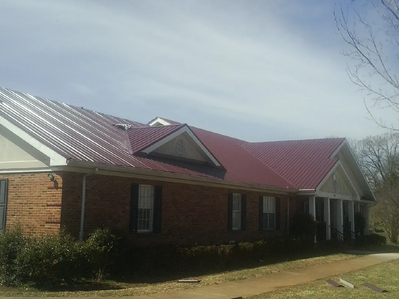 Red metal roof with gabled entries on a long brick building, from a Hail Damage Roof Repair job in Battle Creek