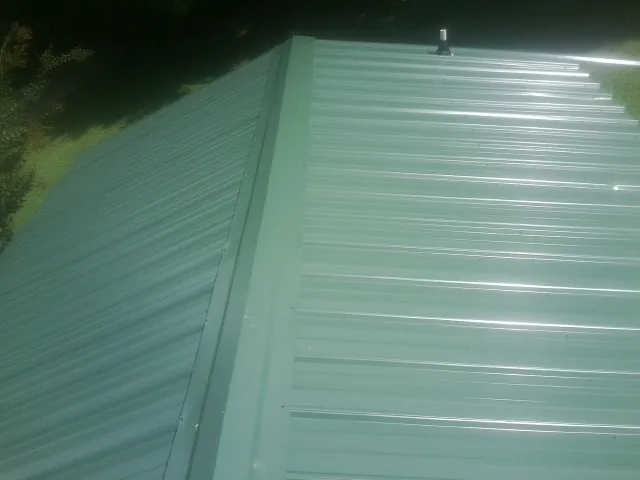 New green metal panels meeting at the ridge of a roof — Flat Roof Repair work by our crew in Battle Creek