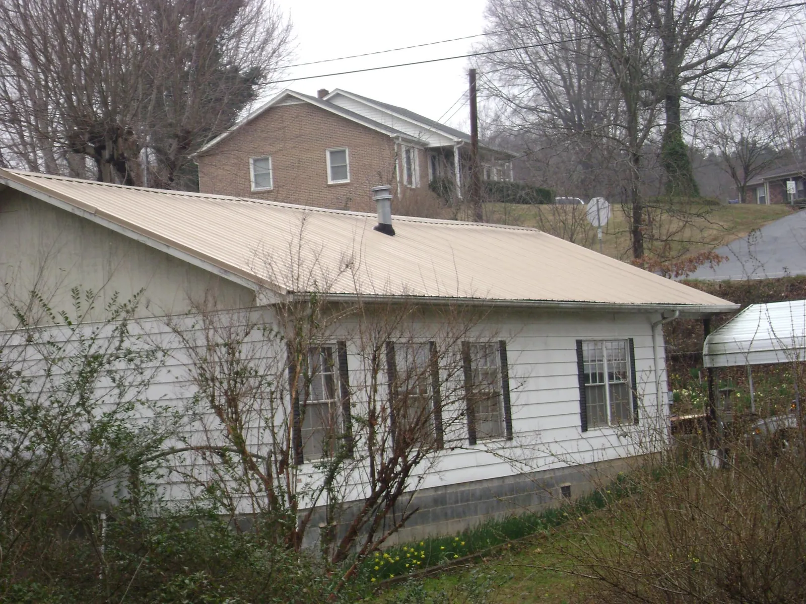 Tan metal roof on a white sided house set into a hillside — Commercial Roofing by Roofing Brothers in Battle Creek