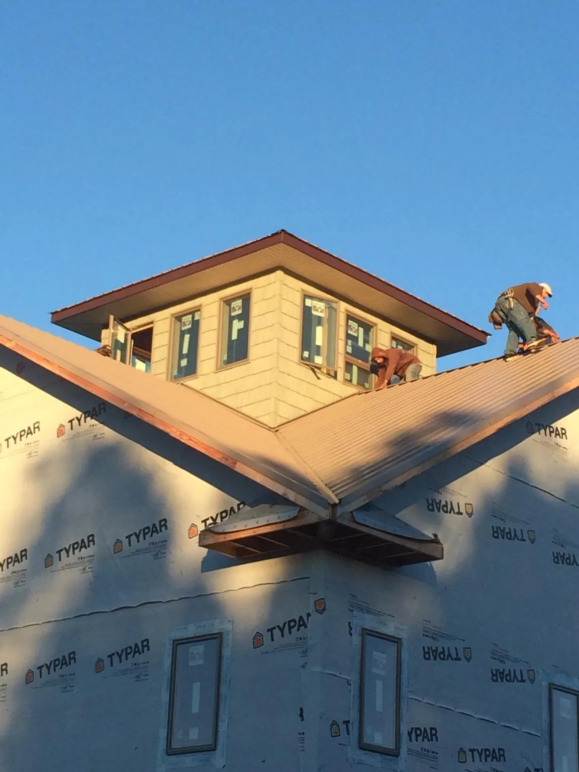 Roofers working around a rooftop cupola on a new metal roof at sunset — Roof Waterproofing in Battle Creek by Roofing Brothers